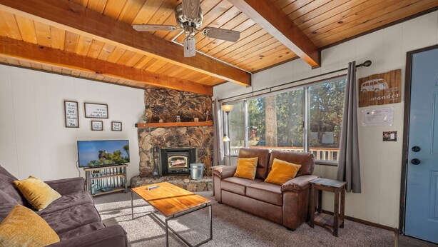 A cozy living room with a stone fireplace, leather sofa, and a television. - Cabin in the Pines (Big Bear Lake)