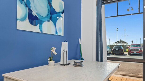 Una habitación con una mesa de madera, un florero blanco con una orquídea, un dispensador de toallas de papel y un cuadro en la pared.