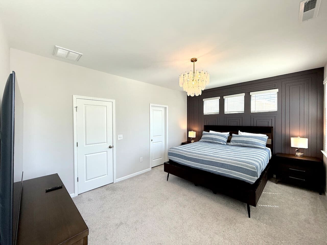 A bedroom with a large bed, two bedside tables, a chandelier, and a door.