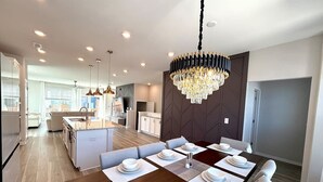 A modern kitchen with a dining area, featuring a large island, pendant lights, and a chandelier. - TPV - Palazzo Di Amore - BRAND NEW - Luxury Living (Durham)