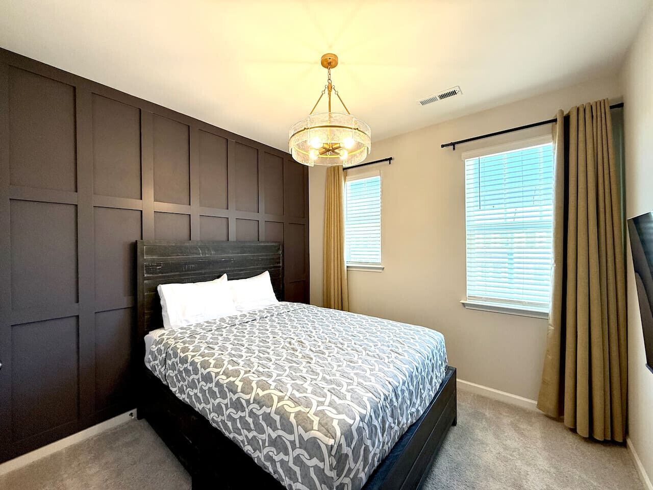 A bedroom with a bed, a ceiling fan, a window with curtains, and a wall-mounted TV.