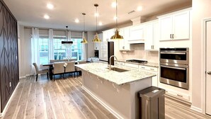 A modern kitchen with a large island, stainless steel appliances, and pendant lighting. - TPV - Palazzo Di Amore - BRAND NEW - Luxury Living (Durham)