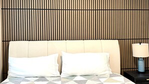 Ein Bett mit geometrisch gemustertem Überwurf, zwei Kissen, einem Kopfteil mit vertikalen Lamellen und einem Nachttisch mit einer Lampe.