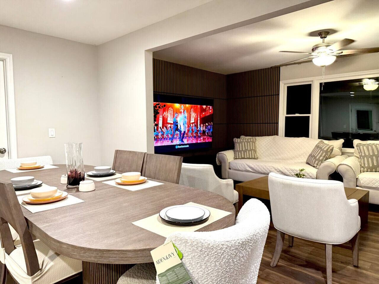 Ein modernes Wohnzimmer mit Essbereich, Fernseher und Deckenventilator.