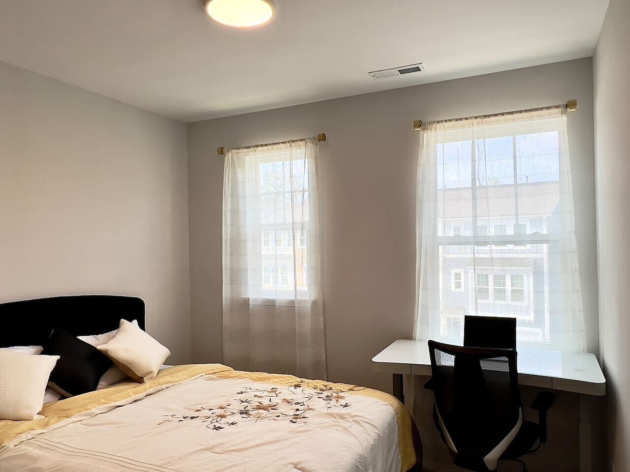 Ein Schlafzimmer mit einem Bett, einem Schreibtisch und zwei Fenstern mit Vorhängen.