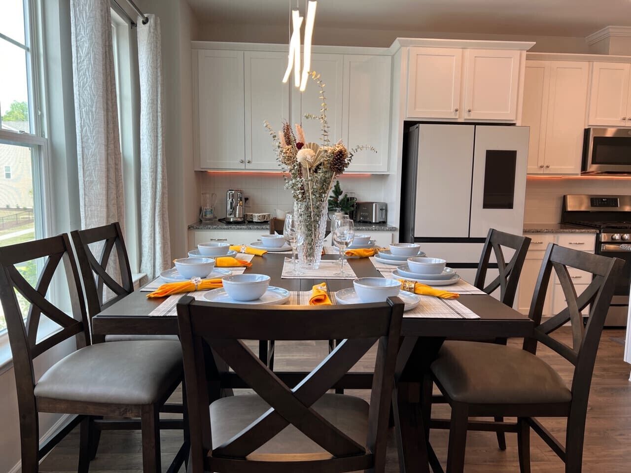 A modern kitchen with white cabinets, a dining table set with plates, bowls, and a vase with flowers.