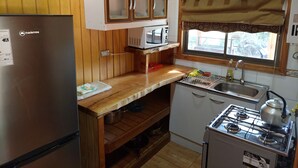 Ett kompakt kök med träpanel, en inbyggd mikrovågsugn, en gasspis och ett handfat.