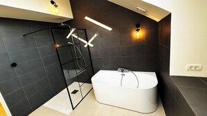 Um banheiro moderno com chuveiro em box de vidro, uma banheira branca e duas luminárias fixadas na parede.