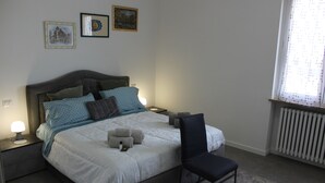 Een netjes opgemaakt bed met een hoofdbord, nachtkastjes met lampen, een stoel en een raam met uitzicht.