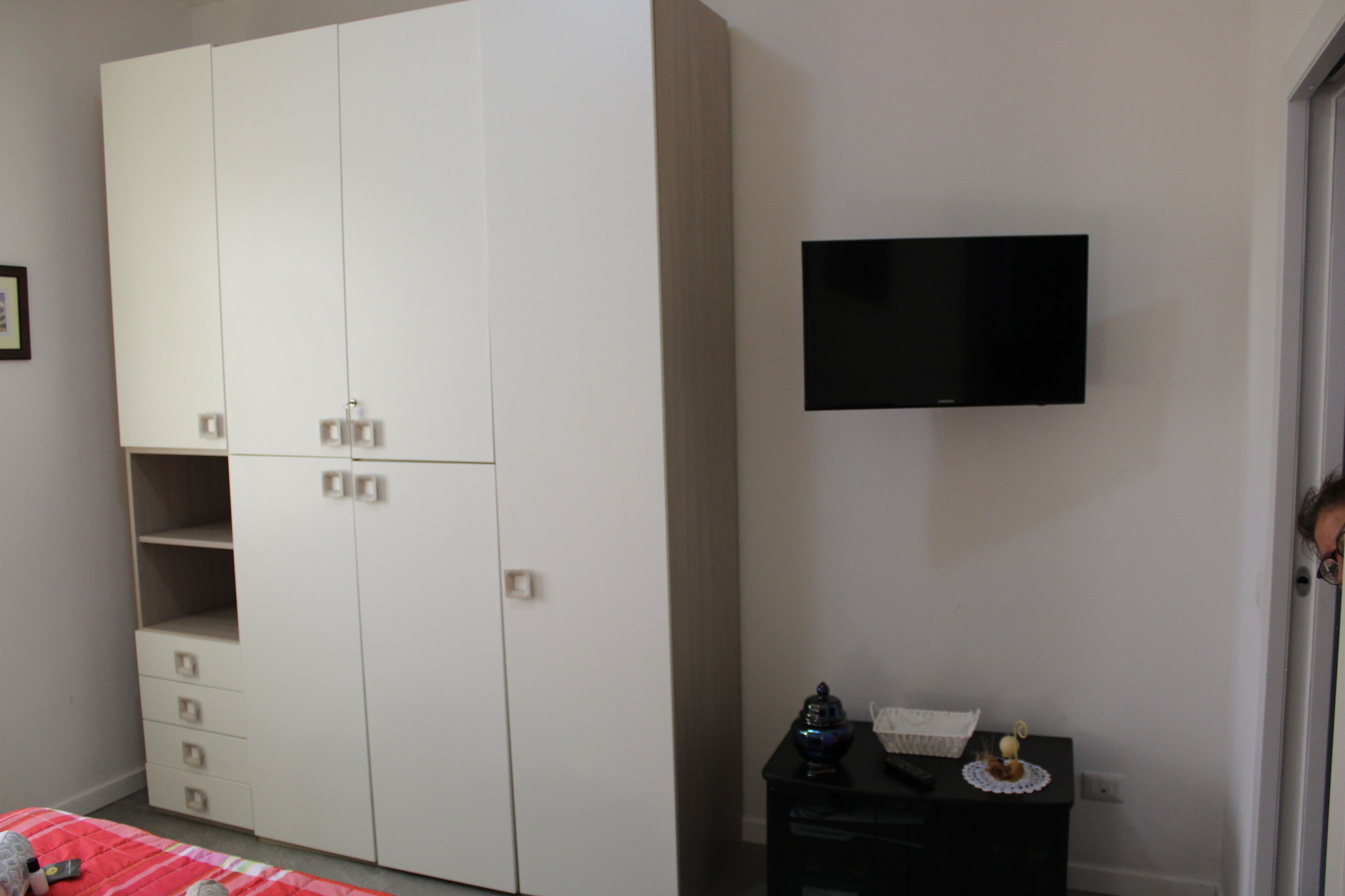 Ein Schlafzimmer mit großem Kleiderschrank, einem kleinen Nachttisch und einem an der Wand befestigten Fernseher.