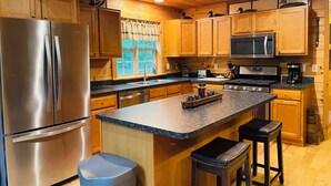 Eine moderne Küche mit Holzschränken, Edelstahlgeräten, einer Arbeitsplatte aus Granit und einer zentralen Kochinsel mit Barhocker.