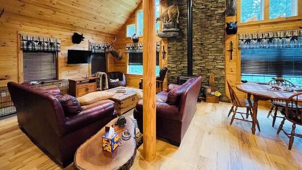 Ein gemütliches Blockhaus-Interieur mit Holzwänden, einem Steinofen, Ledermöbeln und aufgehängten Tierköpfen.