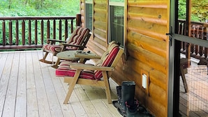 Eine Holzhütte mit Veranda, zwei Stühlen, einem Tisch und einem Deckenventilator.