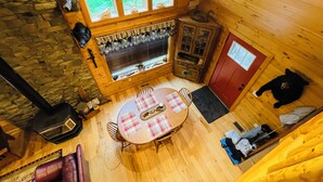 Ein Holzblockhaus-Interieur mit einer Steinwand, einem Kamin, einem Esstisch mit Stühlen, einer roten Tür und einer Bärenstatue.