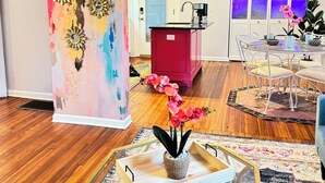 Una sala de estar con un cuadro abstracto grande, una estación de café, un comedor con sillas y una mesa, y un ventilador de techo.