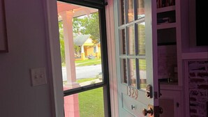 Una puerta con el número 1329, un vitral arriba y vista de una casa amarilla afuera.
