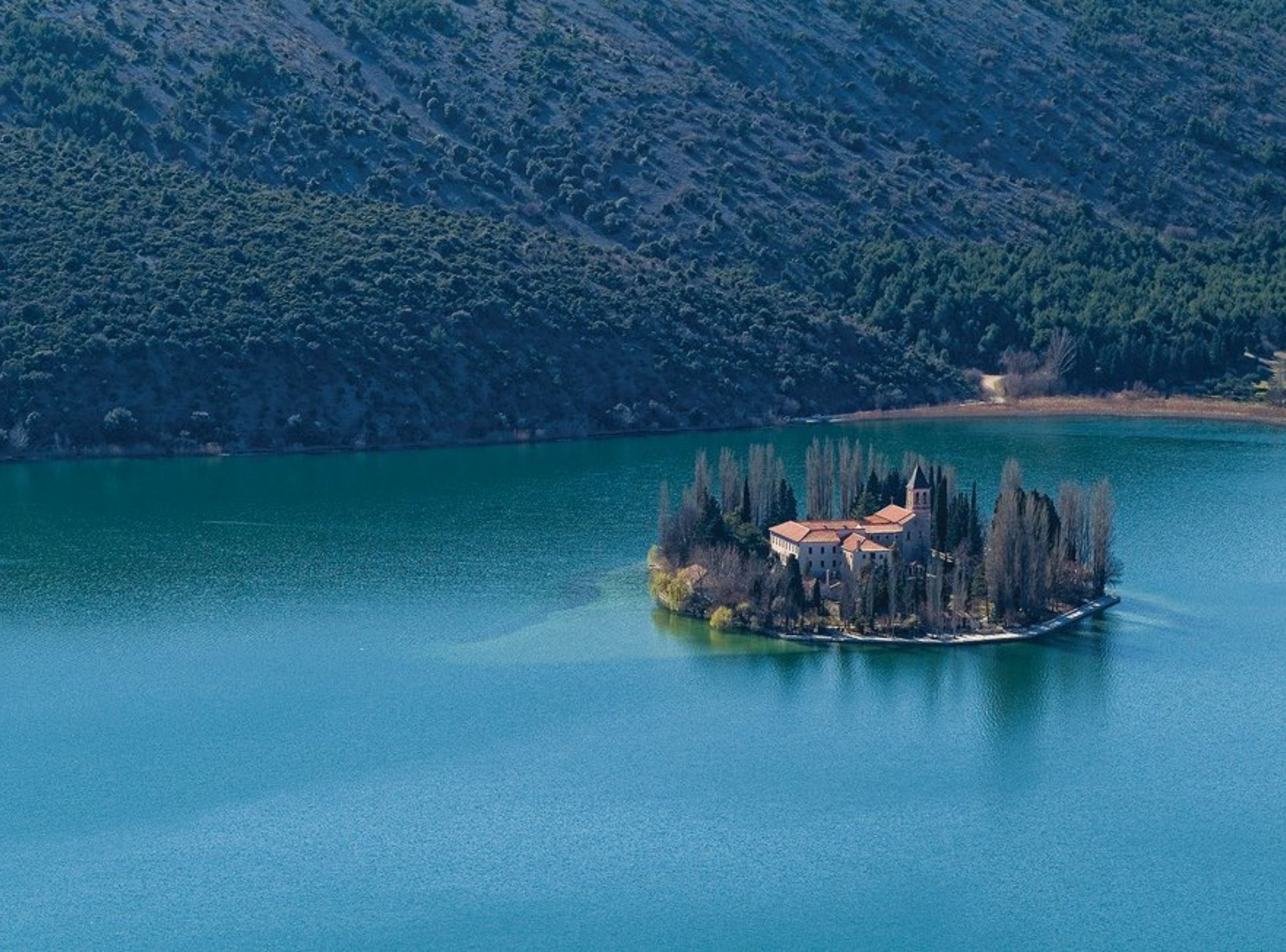 Une petite île avec un bâtiment entouré d’arbres et un lac.