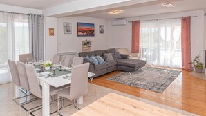 Uma sala de estar moderna com área de jantar, um sofá modular cinza e uma mesa de jantar para quatro pessoas.
