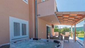 Uma banheira de hidromassagem com pérgola e área de estar ao ar livre, piscina e vista para a paisagem.