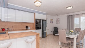 Cozinha moderna com armários brancos, bancada de madeira e área de jantar com mesa posta para quatro pessoas.