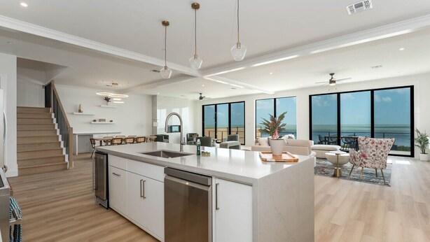 A modern kitchen with a central island, a dining area with a view, and a staircase leading to another level. - 4,000 SF Waterfront Home w/ Pool, Sleeps 22 (Port Isabel)