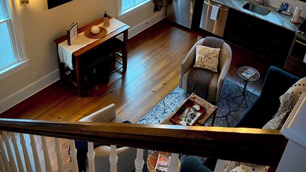 A spacious living area with a high ceiling, wooden beams, a chandelier, a dining table, and a kitchen in the background. - Cozy Upscale Savannah carriage house, walk to all! (Savannah)