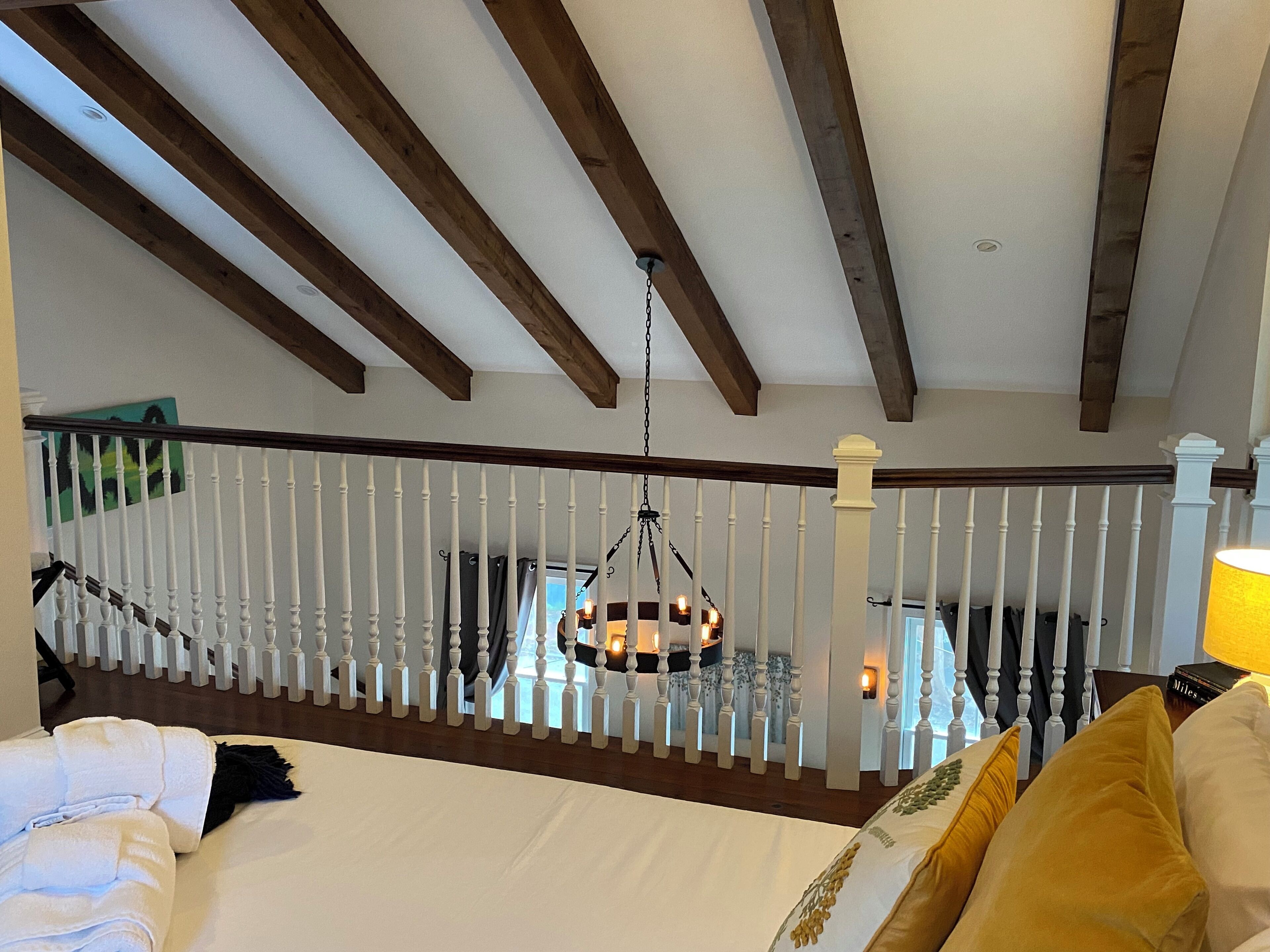 A bedroom with a wooden ceiling, white railing, and a hanging light fixture.