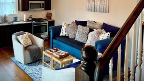 A spacious living area with a blue sofa, a wooden staircase, and a kitchen in the background. - Cozy Upscale Savannah carriage house, walk to all! (Savannah)