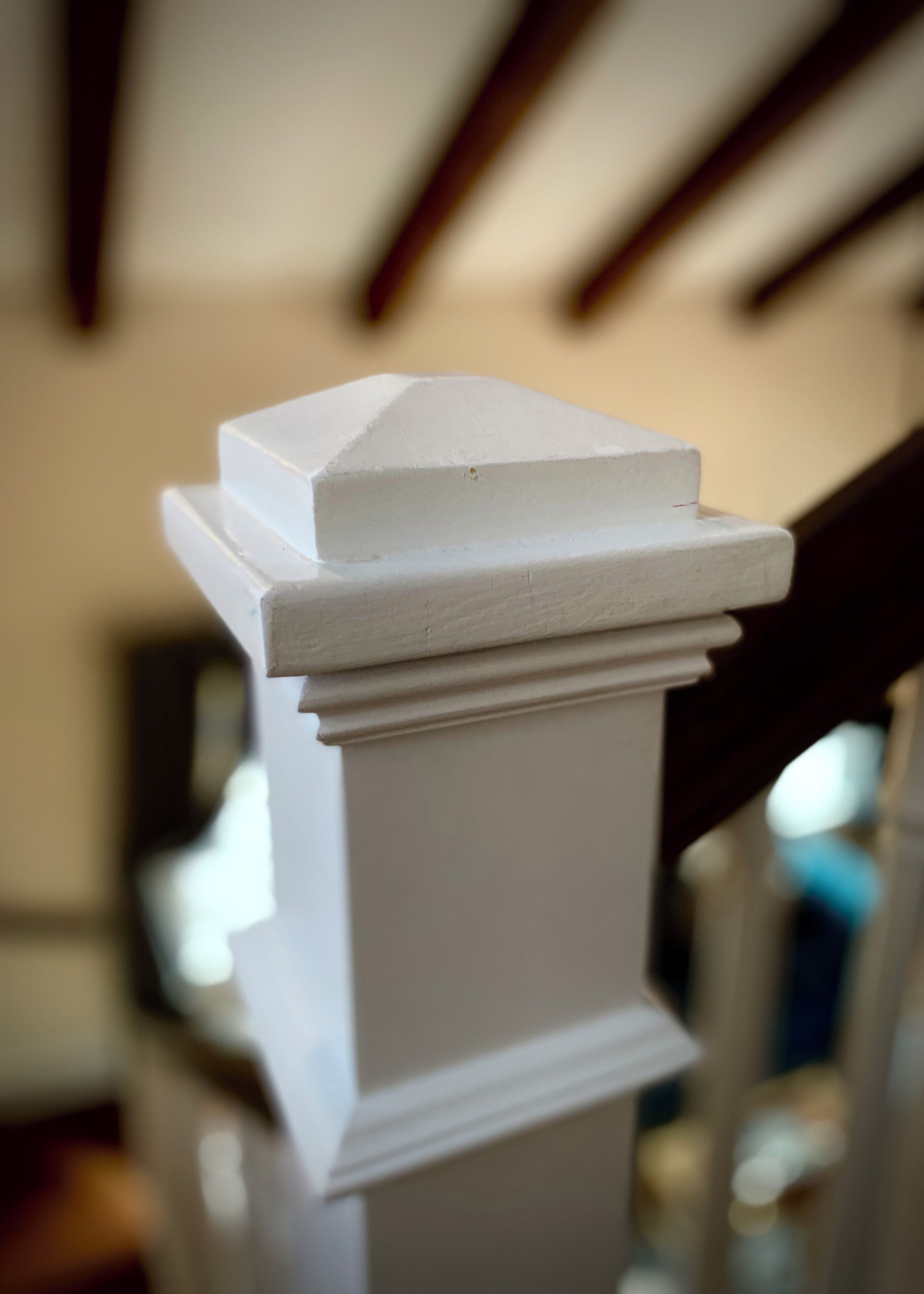 A white, ornate balustrade with a triangular top and a flat base, part of a staircase railing.