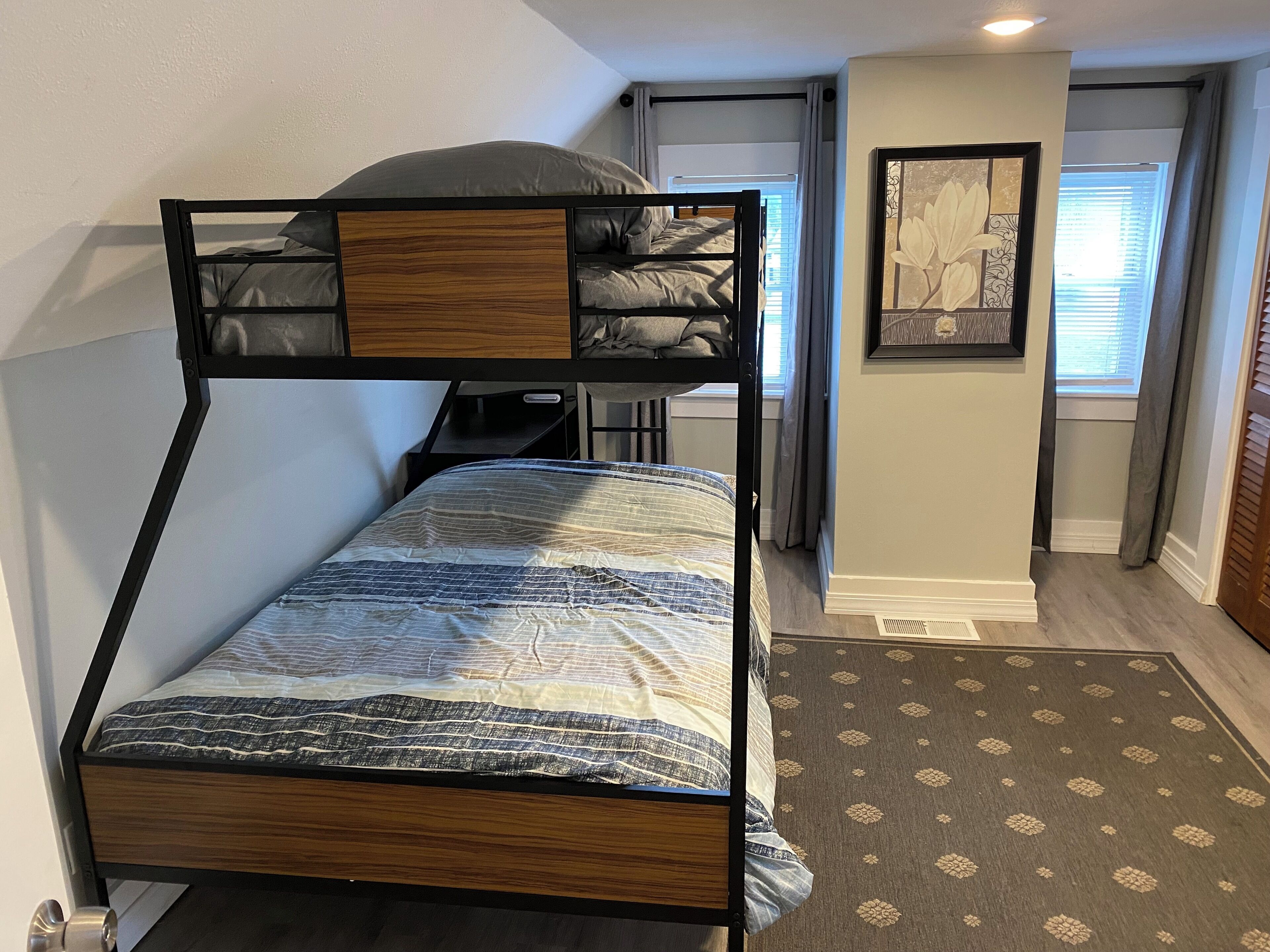 A bunk bed with a wooden headboard and a desk in a room with a patterned rug and a framed picture on the wall.