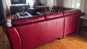 A living room with a red leather sofa, a flat-screen TV, a wooden coffee table, and a small side table. - Peaceful Meredith Getaway - 2 BR w/ Wifi & Charm (Meredith)