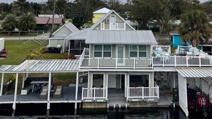 Ein zweistöckiges Haus am Wasser mit einer überdachten Terrasse und mehreren Balkonen.