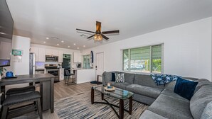 A modern living room with a gray sofa, a glass coffee table, and a dining area with a dark wooden table and chairs.