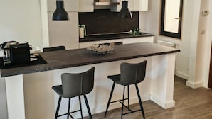 A modern kitchen with a central island, two bar stools, pendant lights, and a window. - Isensi luxury suite Trani (Trani)