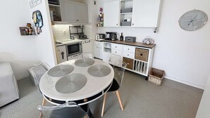 A compact kitchen with white cabinets, a dining table with four chairs, and a clock on the wall. - Charming 1-bed apt, sleeps 4, balcony, parking, wi-fi (Jullouville)