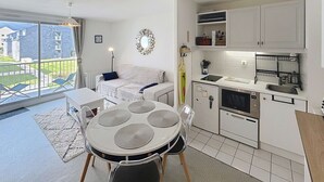 A compact kitchen with white cabinets, a dining table with four chairs, a built-in oven, and a large window offering a view of the outside. - Charming 1-bed apt, sleeps 4, balcony, parking, wi-fi (Jullouville)