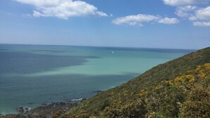A coastal landscape with a clear sky, a view of the sea, and a hilly terrain with vegetation. - Charming 1-bed apt, sleeps 4, balcony, parking, wi-fi (Jullouville)
