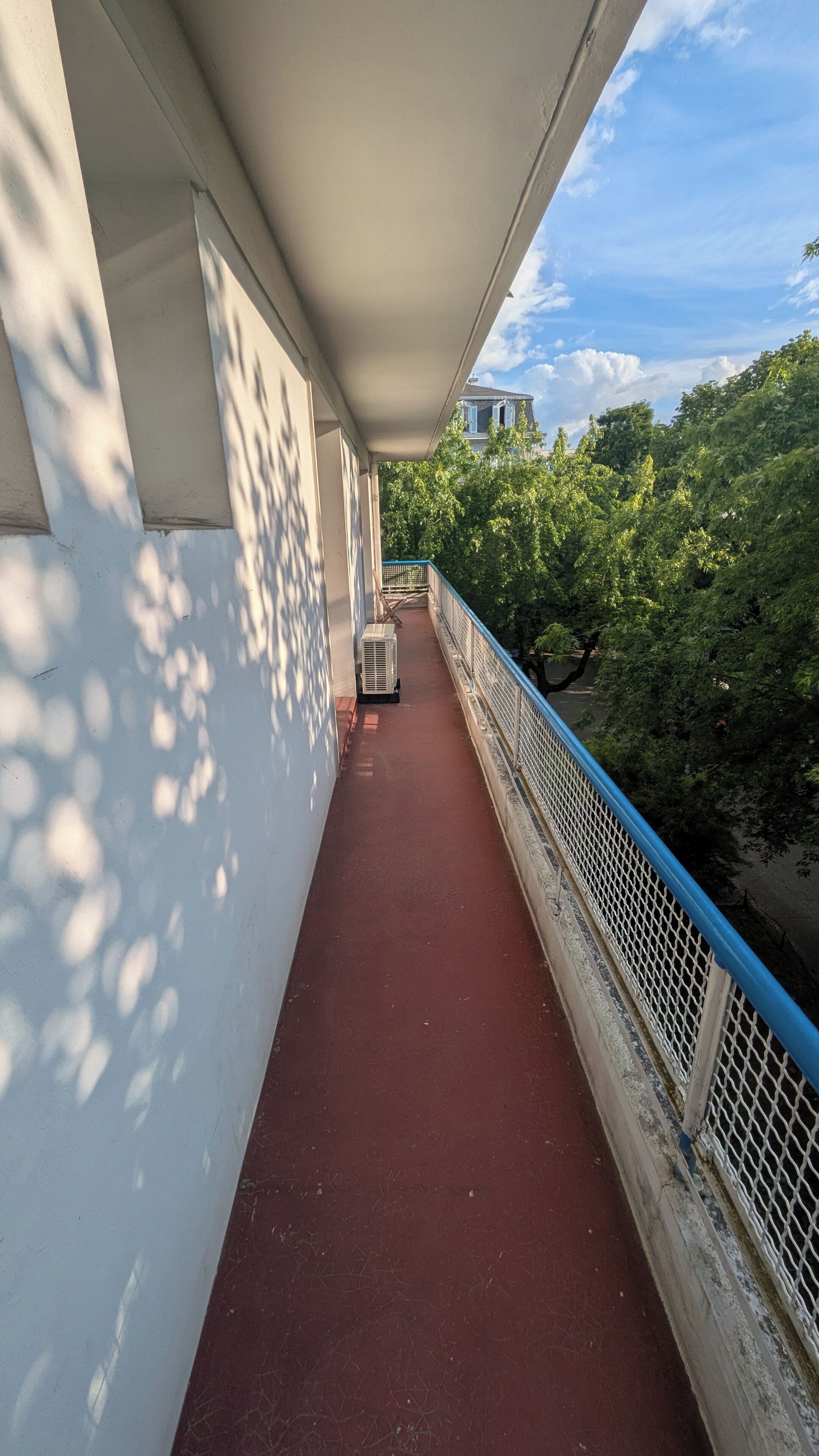 Ein überdachter Balkon mit rotem Boden, weißen Wänden und einem blauen Geländer.
