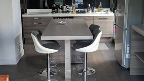 A modern kitchen with a central island, bar stools, a chandelier, and a stainless steel refrigerator.