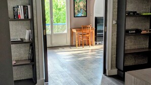 A spacious room with a wooden floor, a dining table with chairs, and a bookshelf.