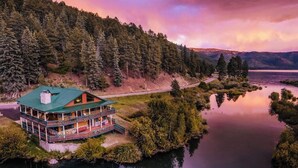 Eine am See gelegene Lodge mit grüner Dachdeckung, umgeben von bewaldeten Hügeln und einem stillen See.