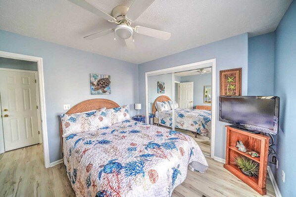 A bedroom with a bed, a ceiling fan, a television, and a mirror.