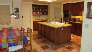 Una cocina con una isla central, armarios de madera y un comedor con mantel colorido.