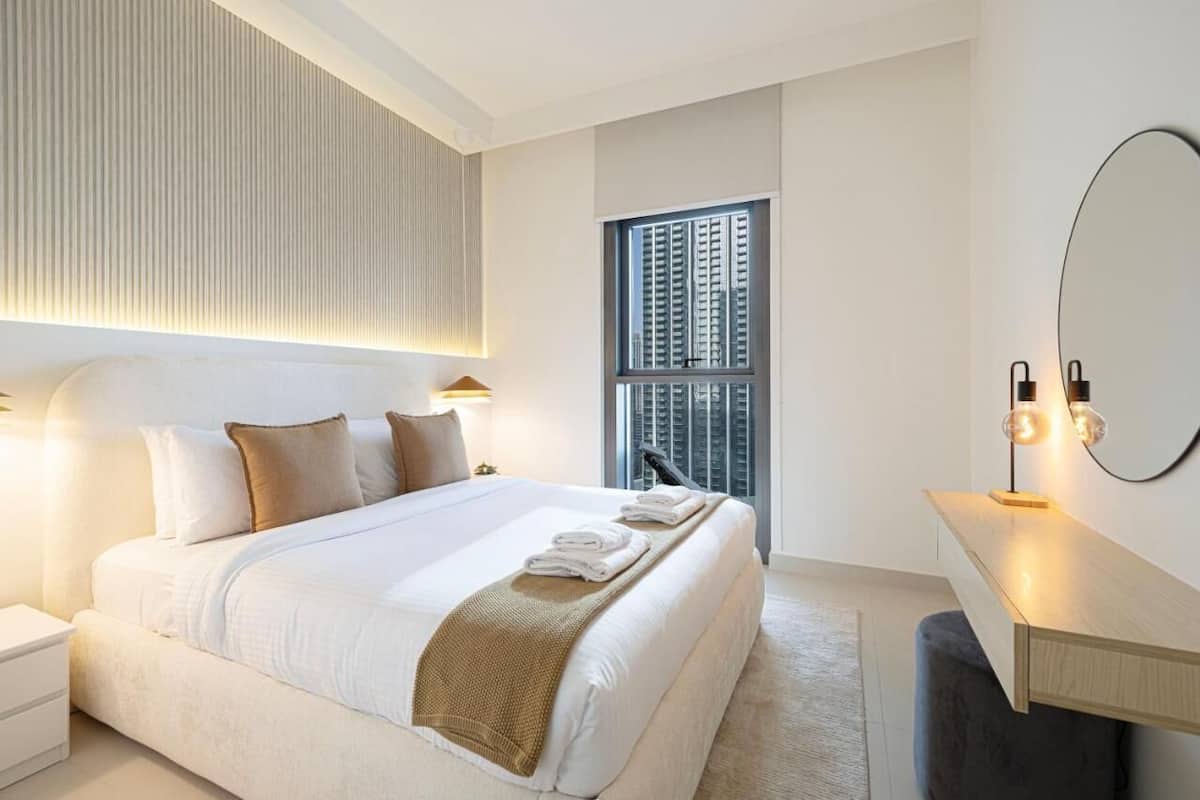Ein modernes Hotelzimmer mit einem großen Bett, Nachttischlampen, einem Schreibtisch mit Spiegel und einem Fenster mit Jalousien.