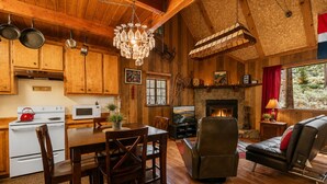 A wooden interior with a dining area, kitchen, fireplace, and seating. - Canyon Cabin (Fawnskin)