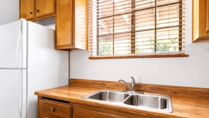 A kitchen with wooden cabinets, a white refrigerator, and a window with blinds. - Canyon Cabin (Fawnskin)
