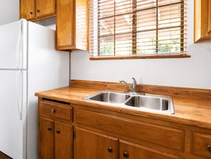 A kitchen with wooden cabinets, a white refrigerator, and a window with blinds. - Canyon Cabin (Fawnskin)