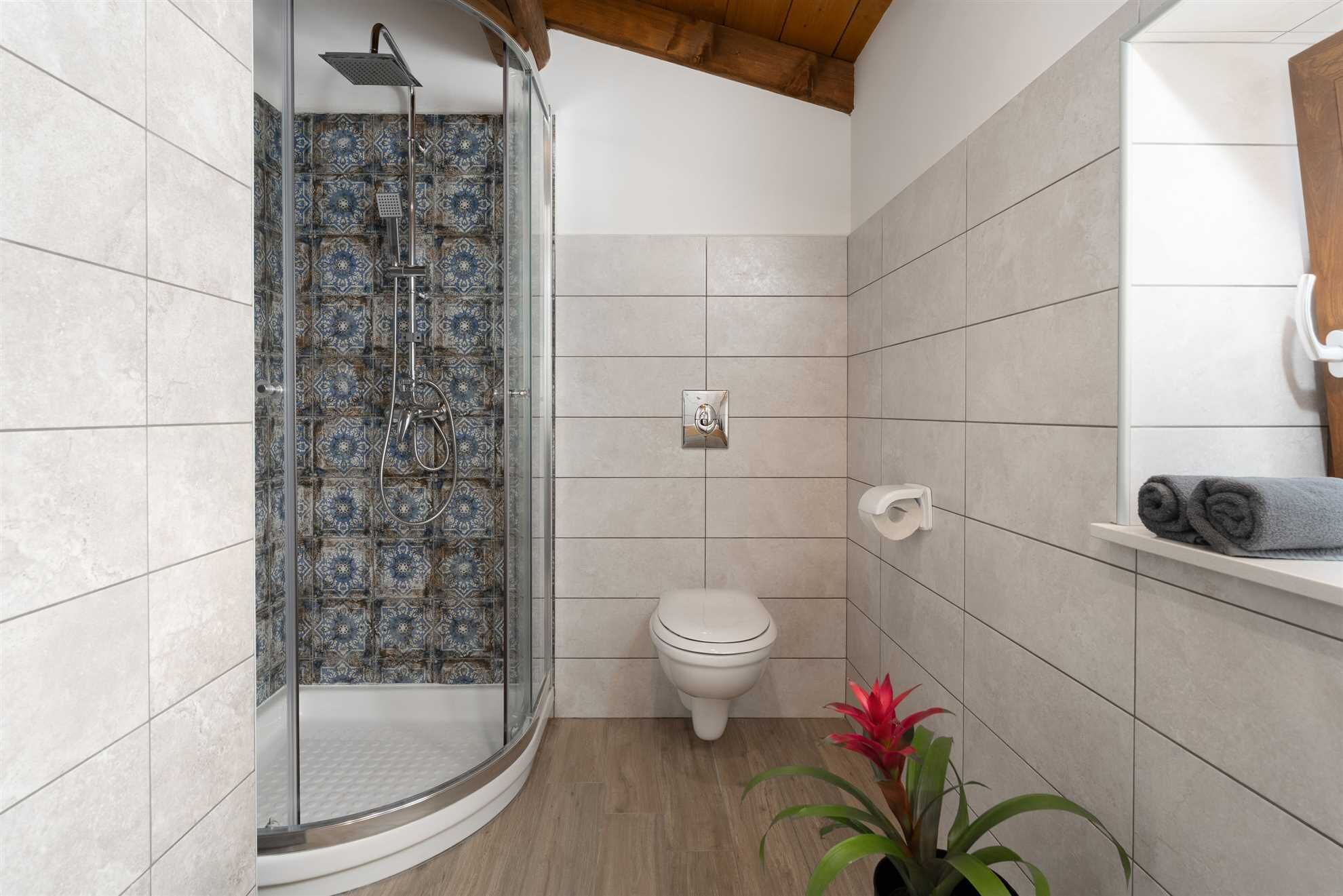 A bathroom with a shower, toilet, and a shelf with towels.