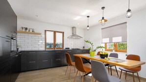 A modern kitchen with dark cabinets, a wooden dining table, and a view of the outdoors through large windows. - Villa Vito an peaceful escape near historic town (Labin)