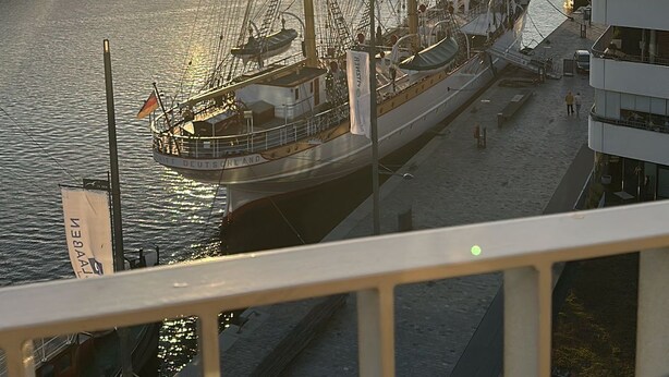 Een haven met hoge schepen in de haven, een heldere lucht en een ondergaande of opkomende zon.